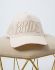 Beige Bride Embroidered Trucker Hat on beige fabric surface for bridal accessories