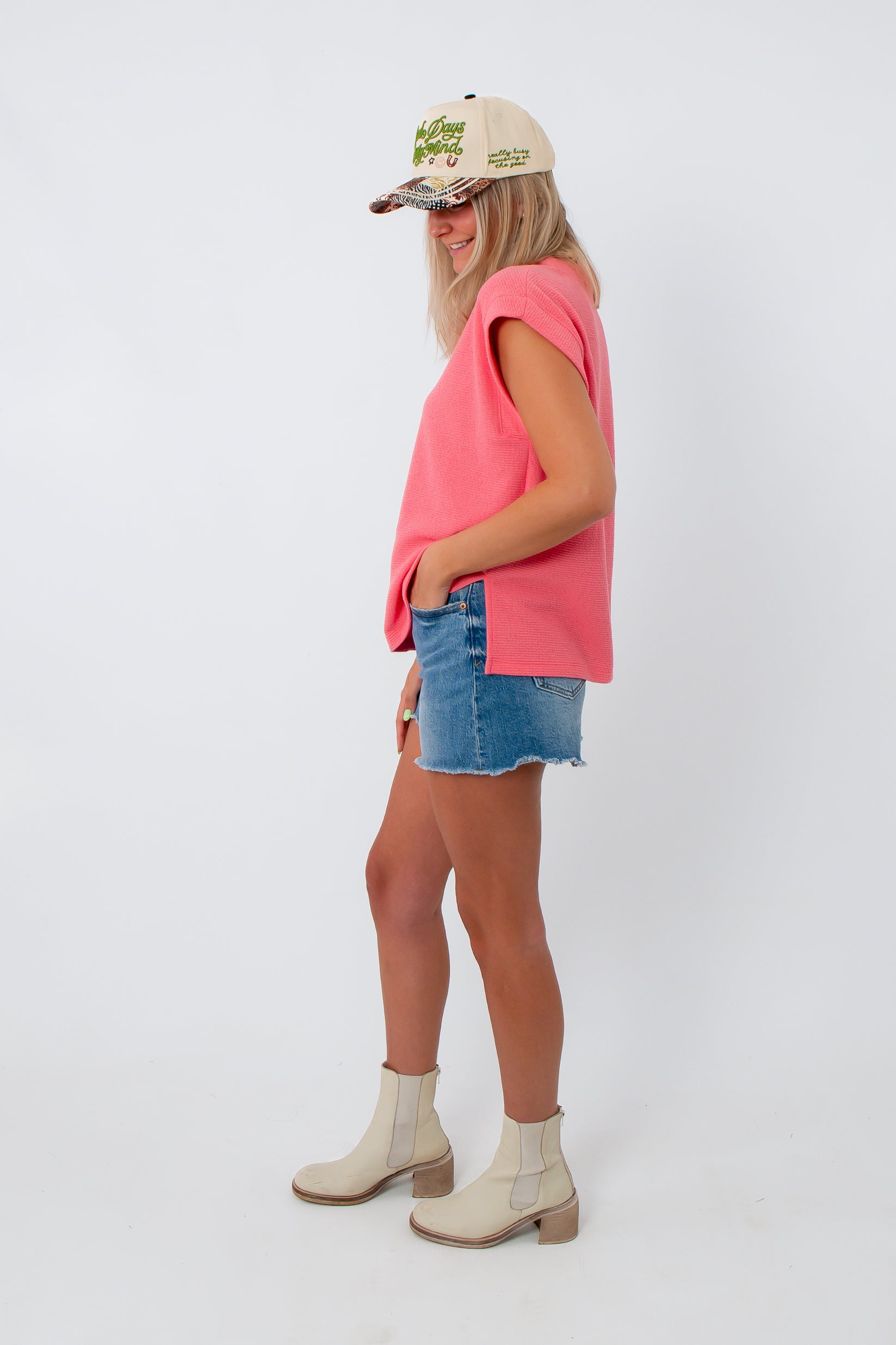 Side view of woman in pink coral knit top, denim shorts, summer fashion