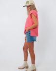 Side view of woman in pink coral knit top, denim shorts, summer fashion
