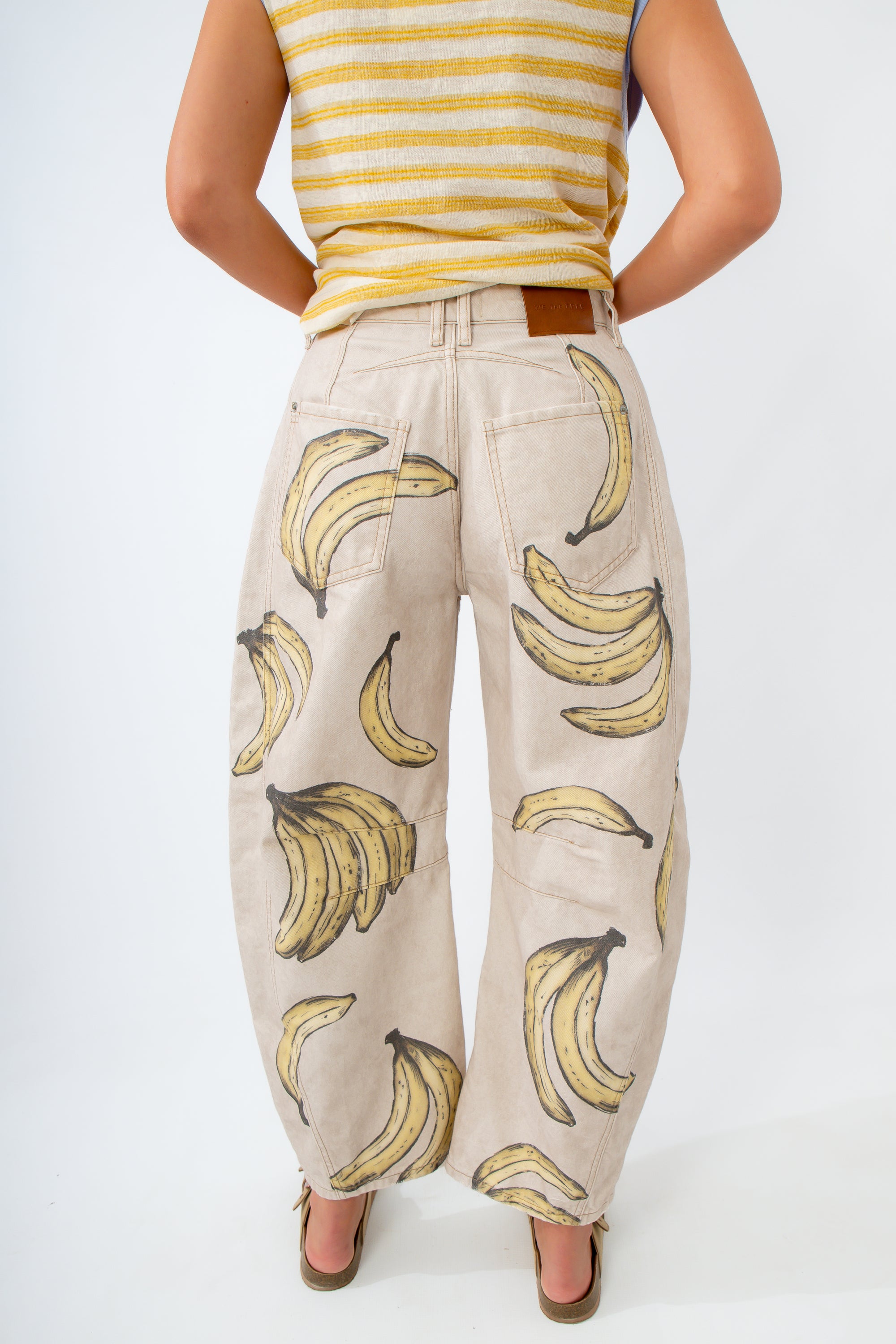 Person wearing a yellow striped top and beige pants with banana pattern on a white background