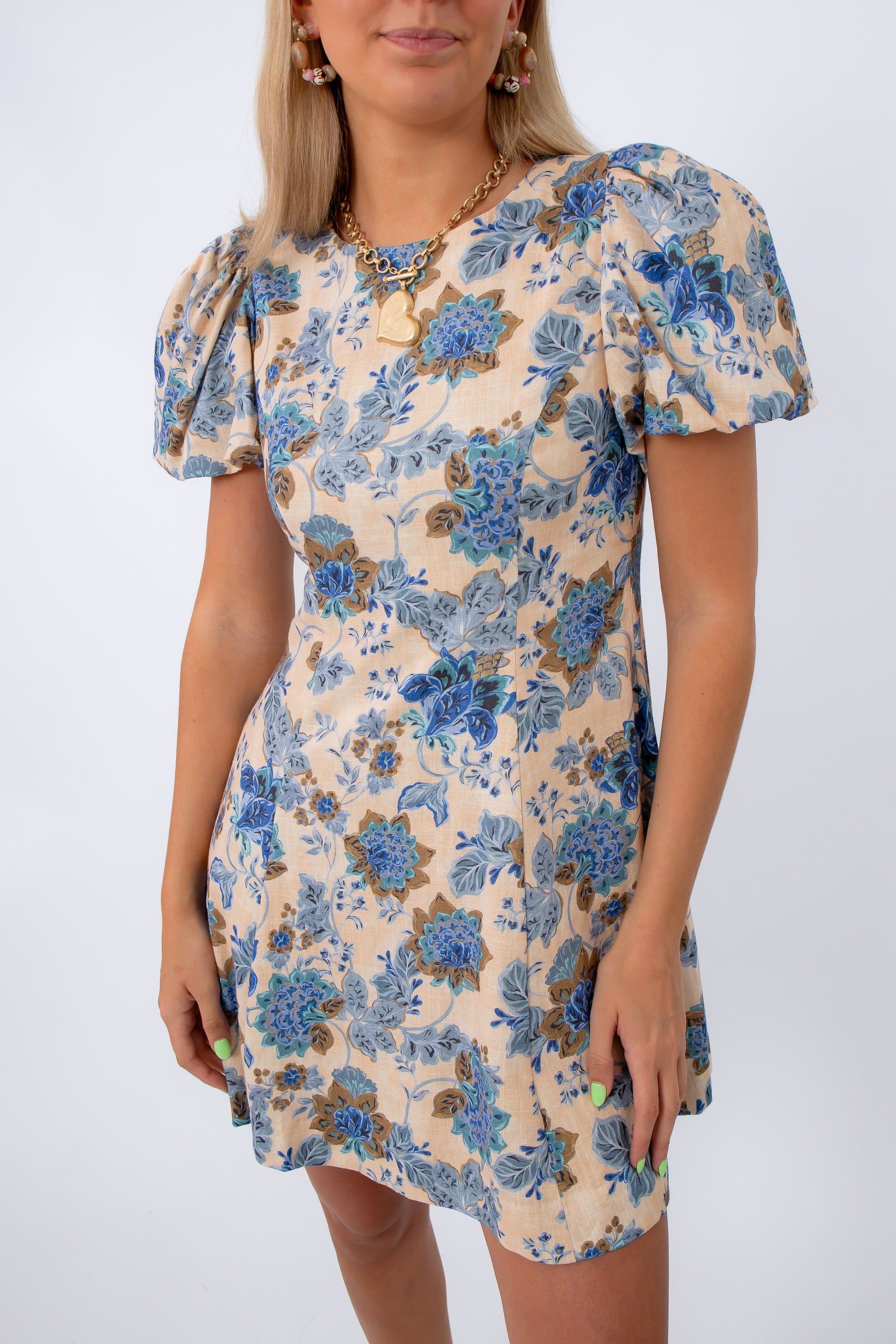 Close-up of floral dress with puff sleeves, beige background, and blue flower pattern, styled with jewelry
