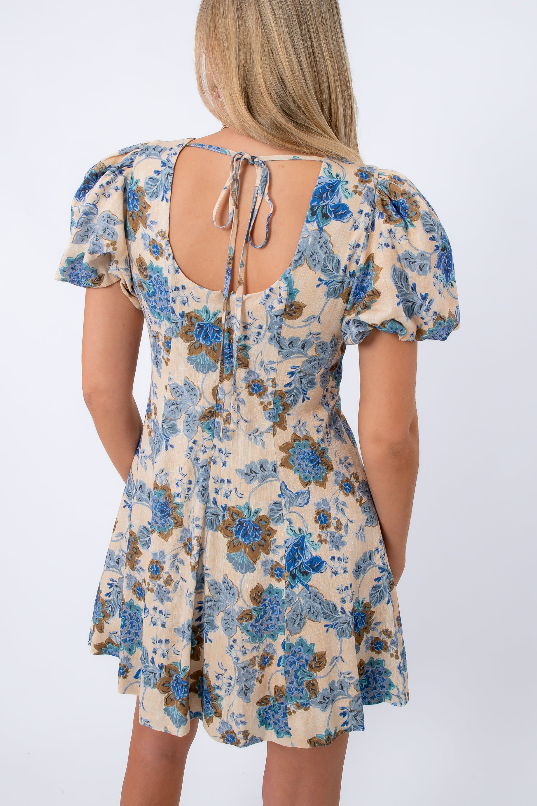 Back view of floral mini dress with open back and tie detail, beige and blue print, women's summer dress