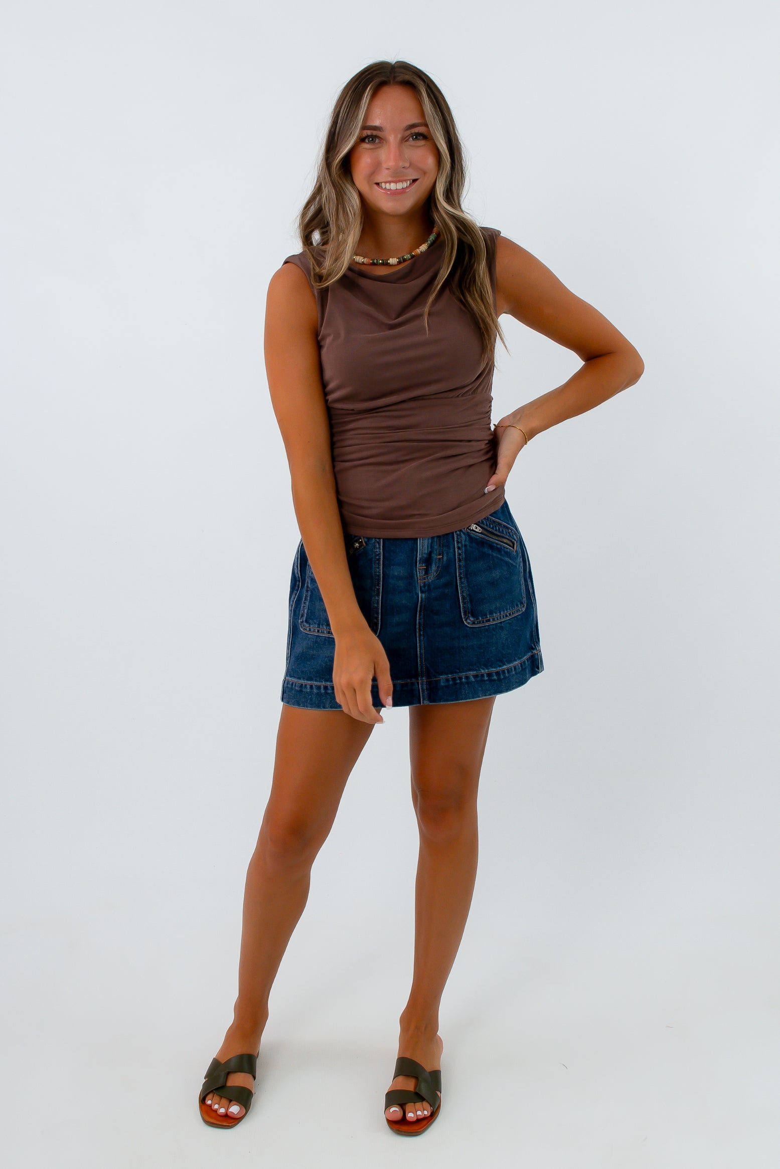 Dark wash denim mini skirt with zipper pockets paired with brown cowl neck sleeveless top, 