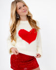 Cupid Crush Heart Cropped Sweater in white knit with bold red heart design, styled with red sequin skirt for Valentine's Day fashion.