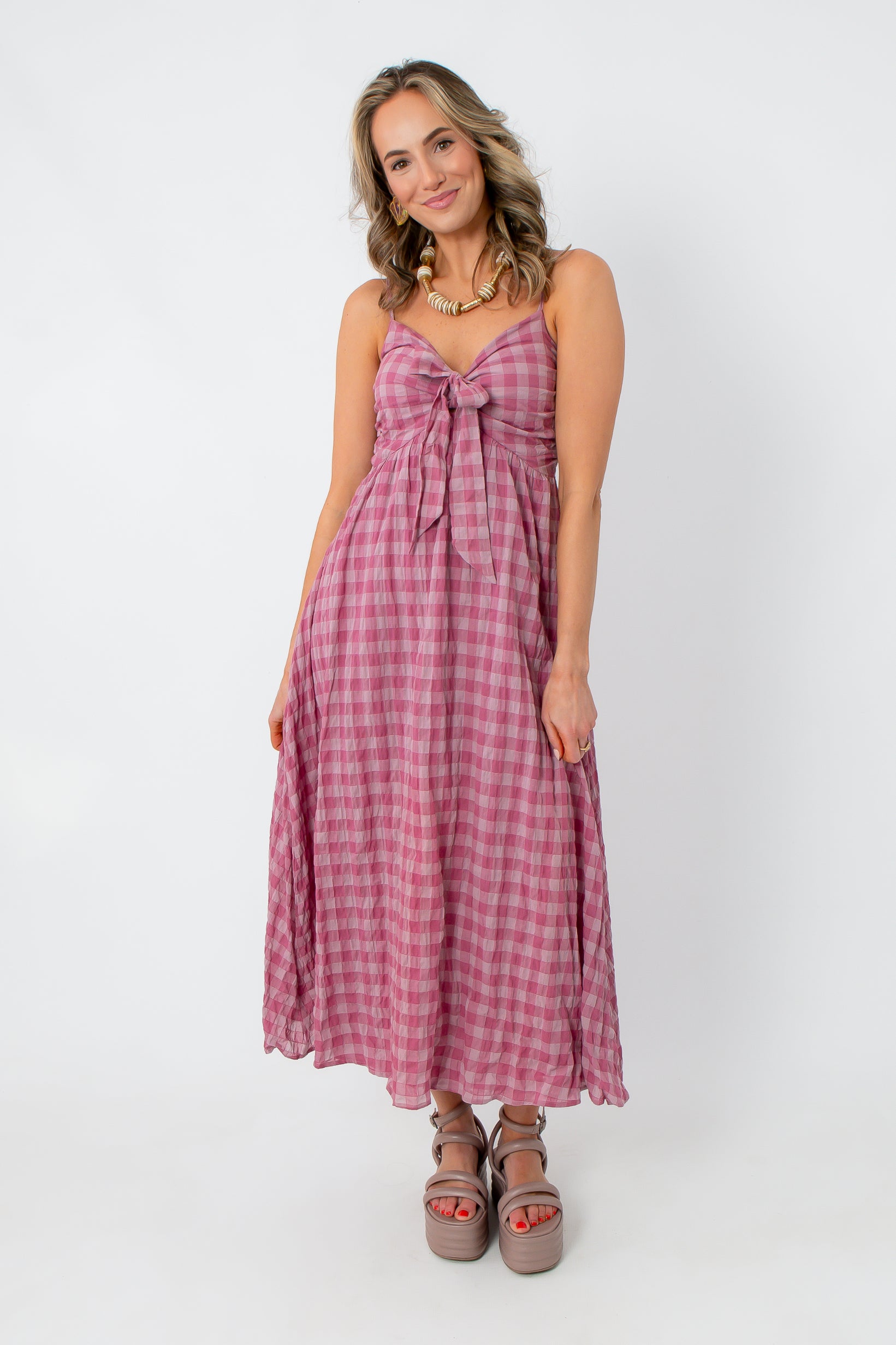 Close-up of pink gingham midi dress with front tie, worn with gold jewelry and a pearl handbag