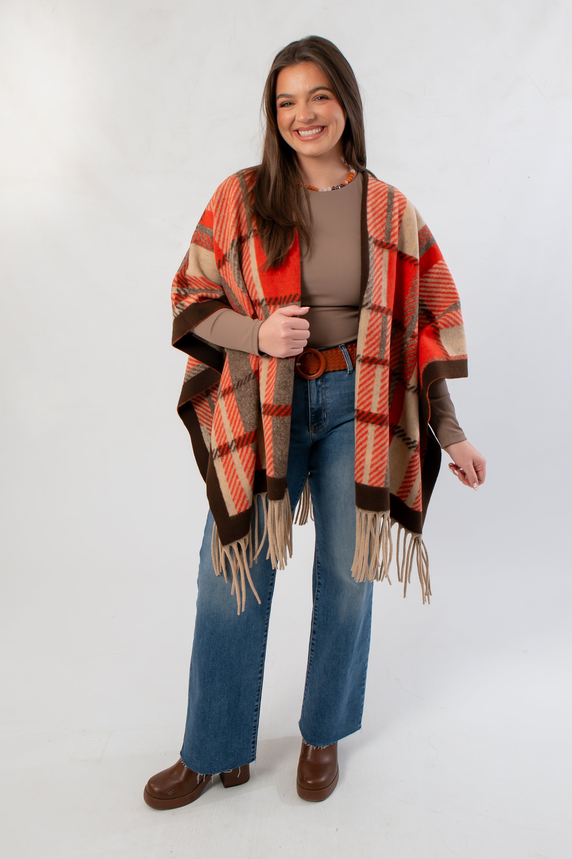 Cozy orange plaid wrap poncho with fringe, perfect for autumn layering, shown styled with wide-leg jeans and brown boots.