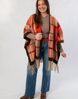 Cozy orange plaid wrap poncho with fringe, perfect for autumn layering, shown styled with wide-leg jeans and brown boots.