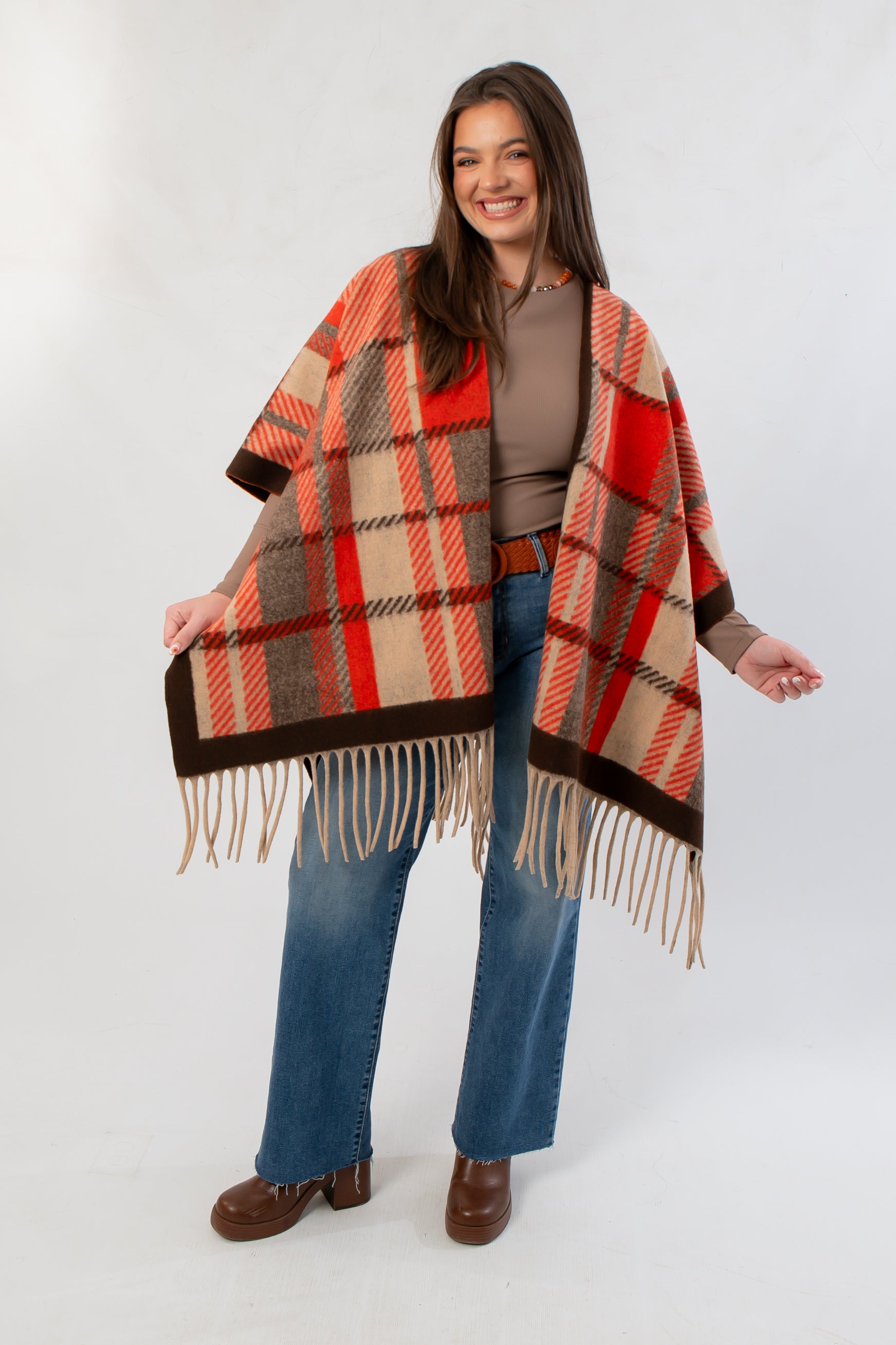 Fireside Plaid Shawl draped over shoulders, showcasing its vibrant orange plaid pattern and fringe hem for a cozy fall look.