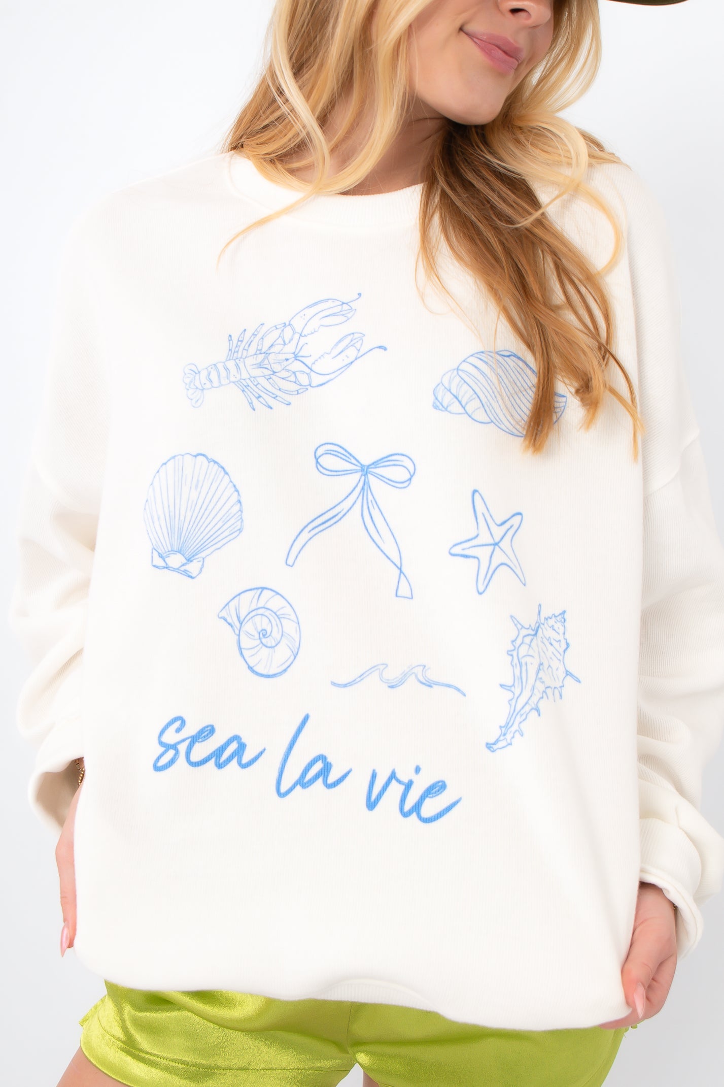 Close-up of Sea La Vie Beach Icons Sweatshirt featuring detailed blue beach-themed graphics and 'sea la vie' text on soft white fabric.