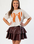 Bone Bow Football Crop Tshirt with bold orange bow graphic, paired with a maroon ruffle skirt for a trendy game day outfit.