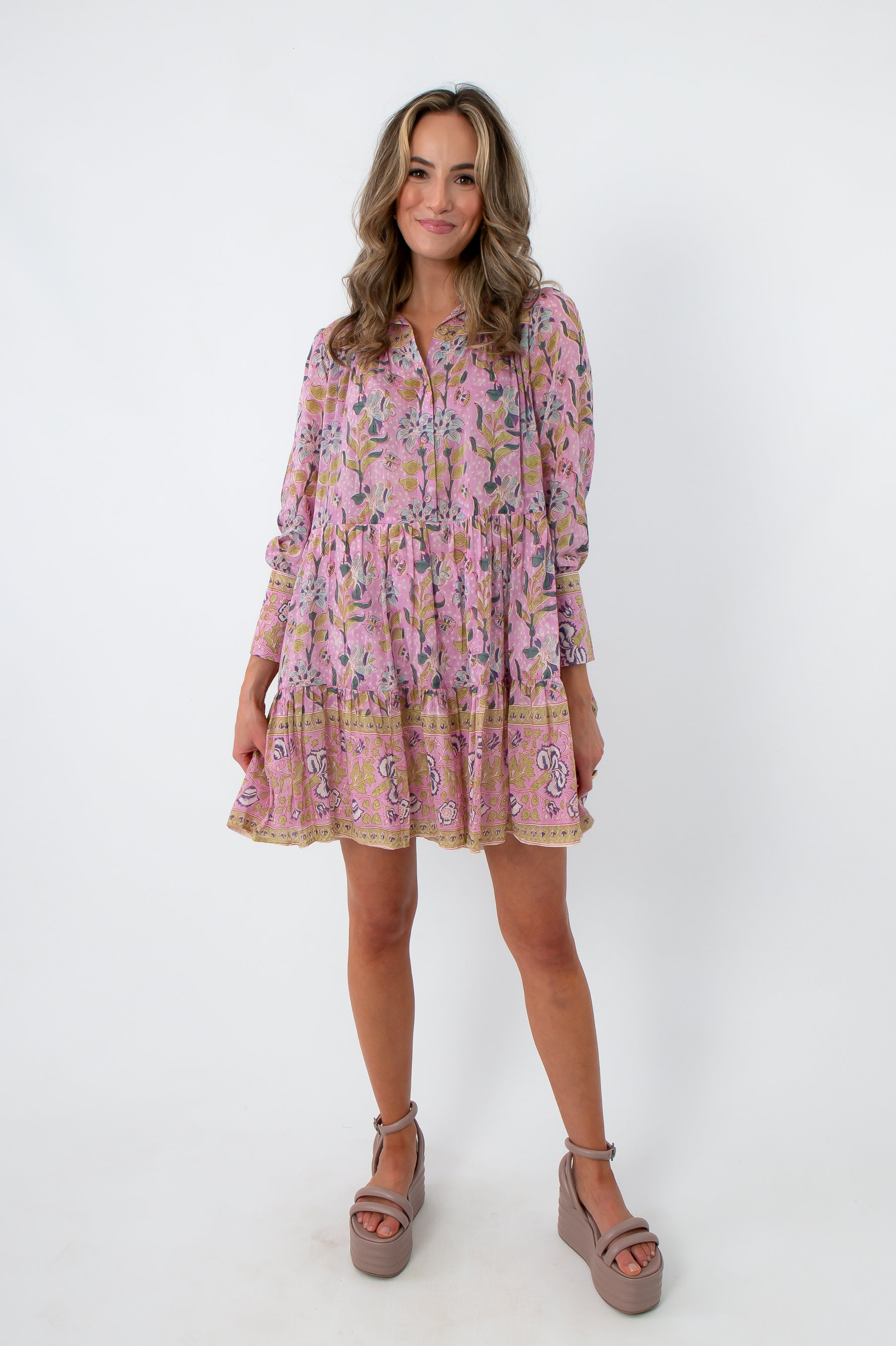Pink floral mini dress with long sleeves, tiered skirt, and pockets, styled with beige platform heels