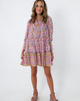Pink floral mini dress with long sleeves, tiered skirt, and pockets, styled with beige platform heels