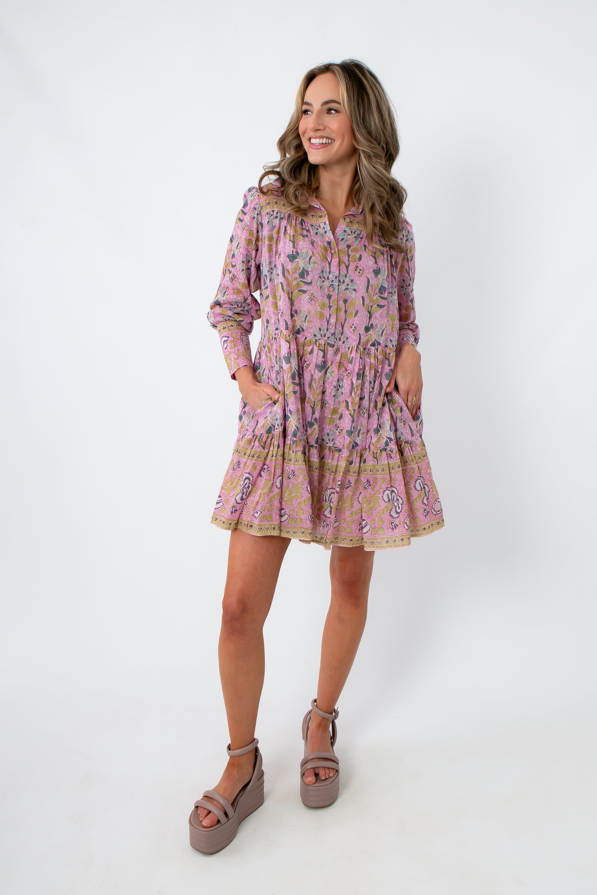 Model wearing pink and purple floral long sleeve mini dress with pockets, styled with beige platform heels and clutch