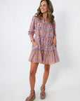 Model wearing pink and purple floral long sleeve mini dress with pockets, styled with beige platform heels and clutch
