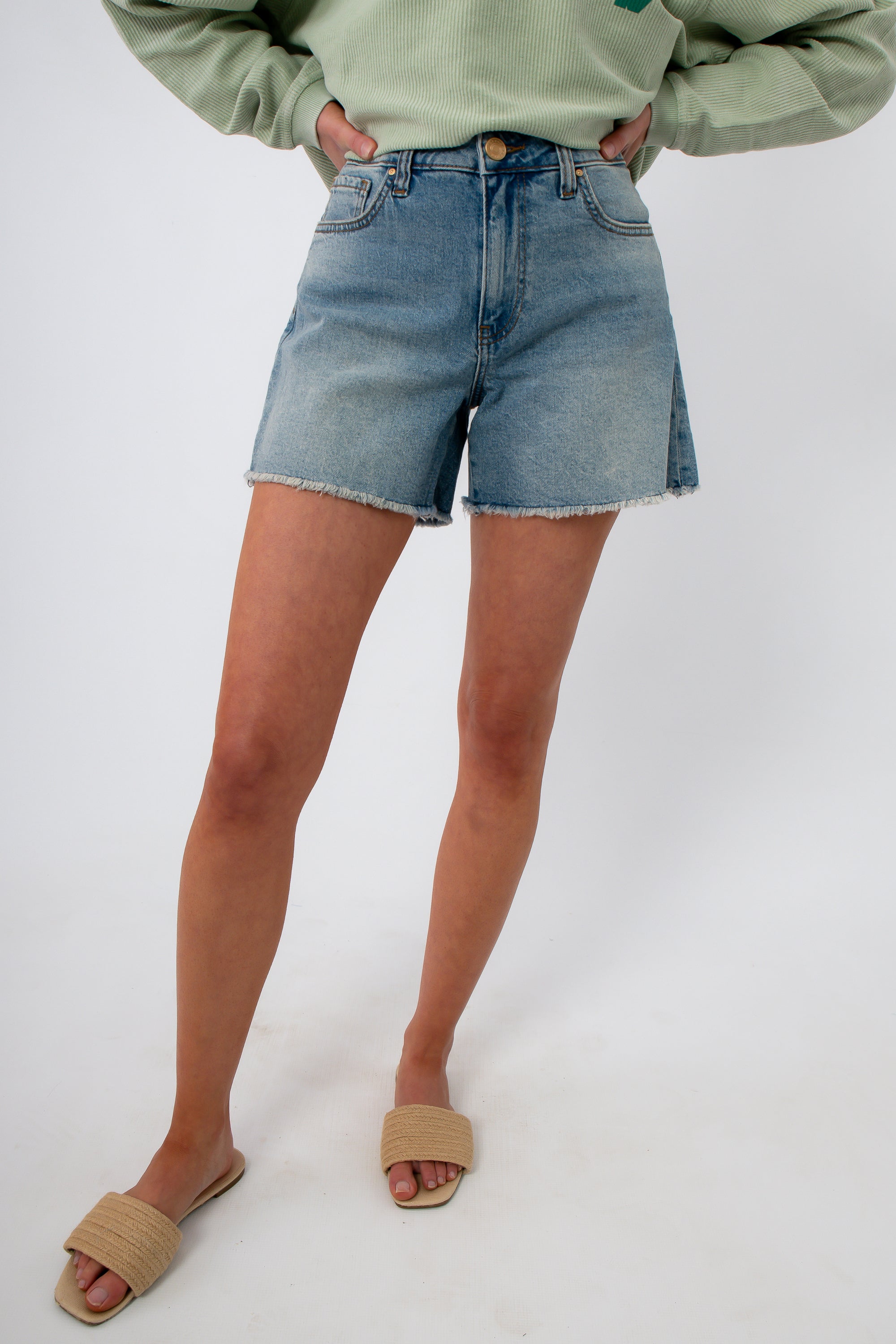 Close-up of high-rise denim shorts with frayed hem, worn with green sweatshirt