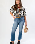 Medium Wash High Rise Crop Flare Jeans styled with a bold patterned top and platform heels. Features a raw hem and flattering high-rise fit.
