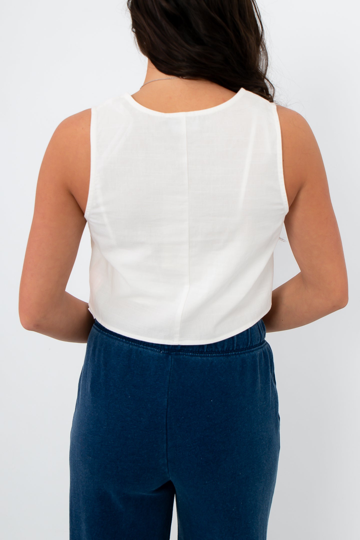 Person wearing a white sleeveless top and blue pants on a plain background