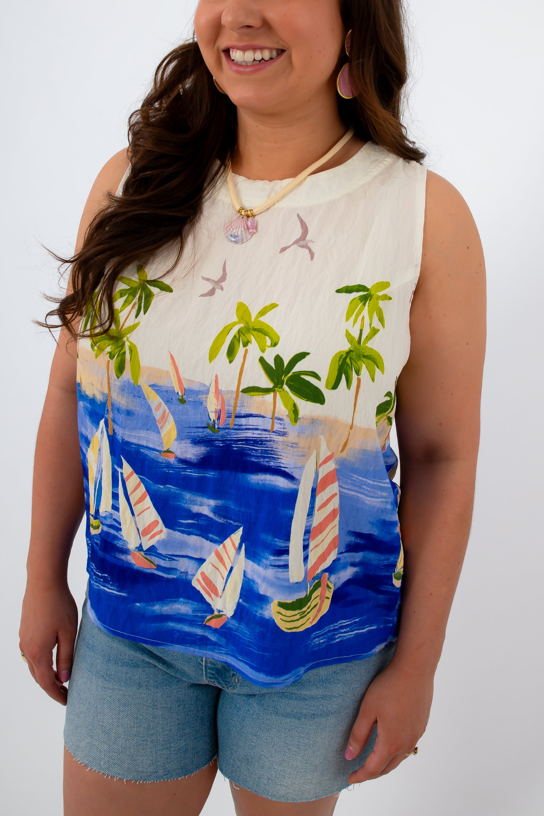 Close-up of woman in tropical sailboat print sleeveless top with palm trees and sailboats, smiling