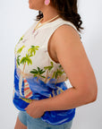 Back view of woman in tropical sailboat print sleeveless top with button closure, denim shorts
