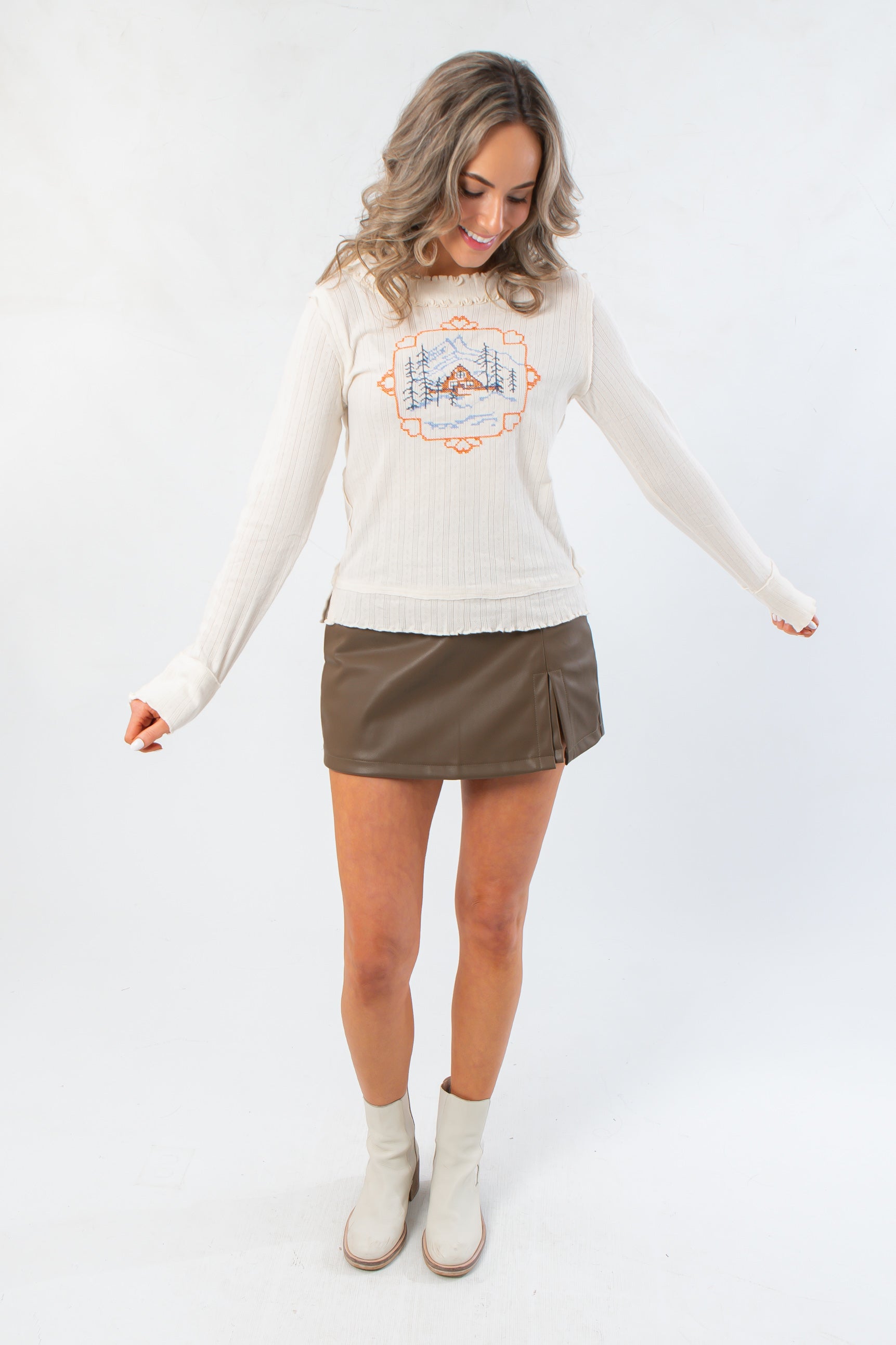 Front view of Free People Through the Woods Tee featuring long sleeves and scenic print, paired with faux leather mini skirt and ankle boots.