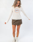 Front view of Free People Through the Woods Tee featuring long sleeves and scenic print, paired with faux leather mini skirt and ankle boots.