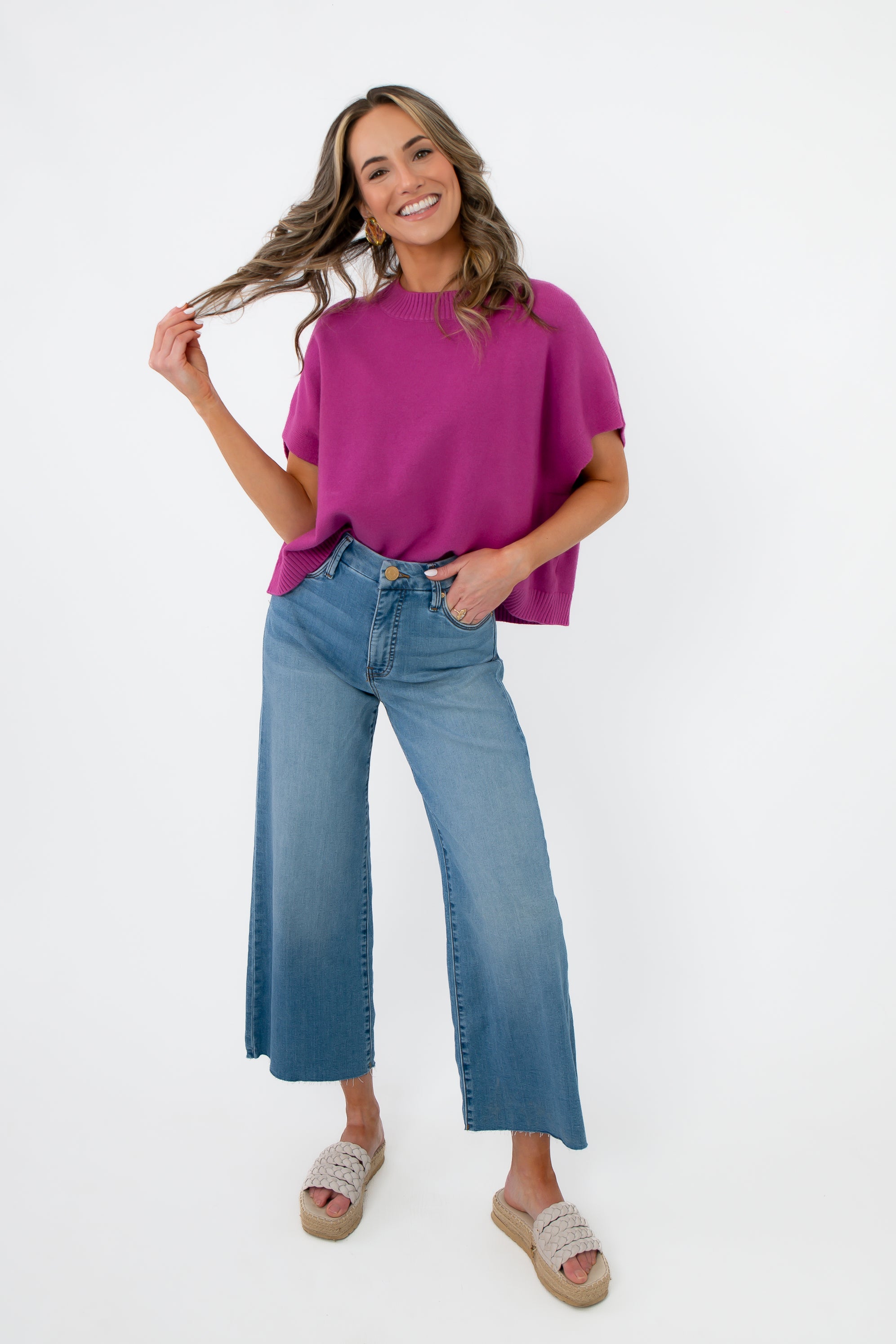 Model wearing Whatever The Weather Orchid Sleeveless Sweater paired with wide-leg jeans and sandals. Stylish purple knit top for casual everyday wear.