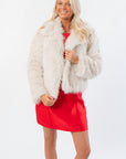 Winter Wonderland Ivory Faux Fur Jacket for women styled over a red holiday dress. Boutique outerwear ideal for winter events and festive layering.