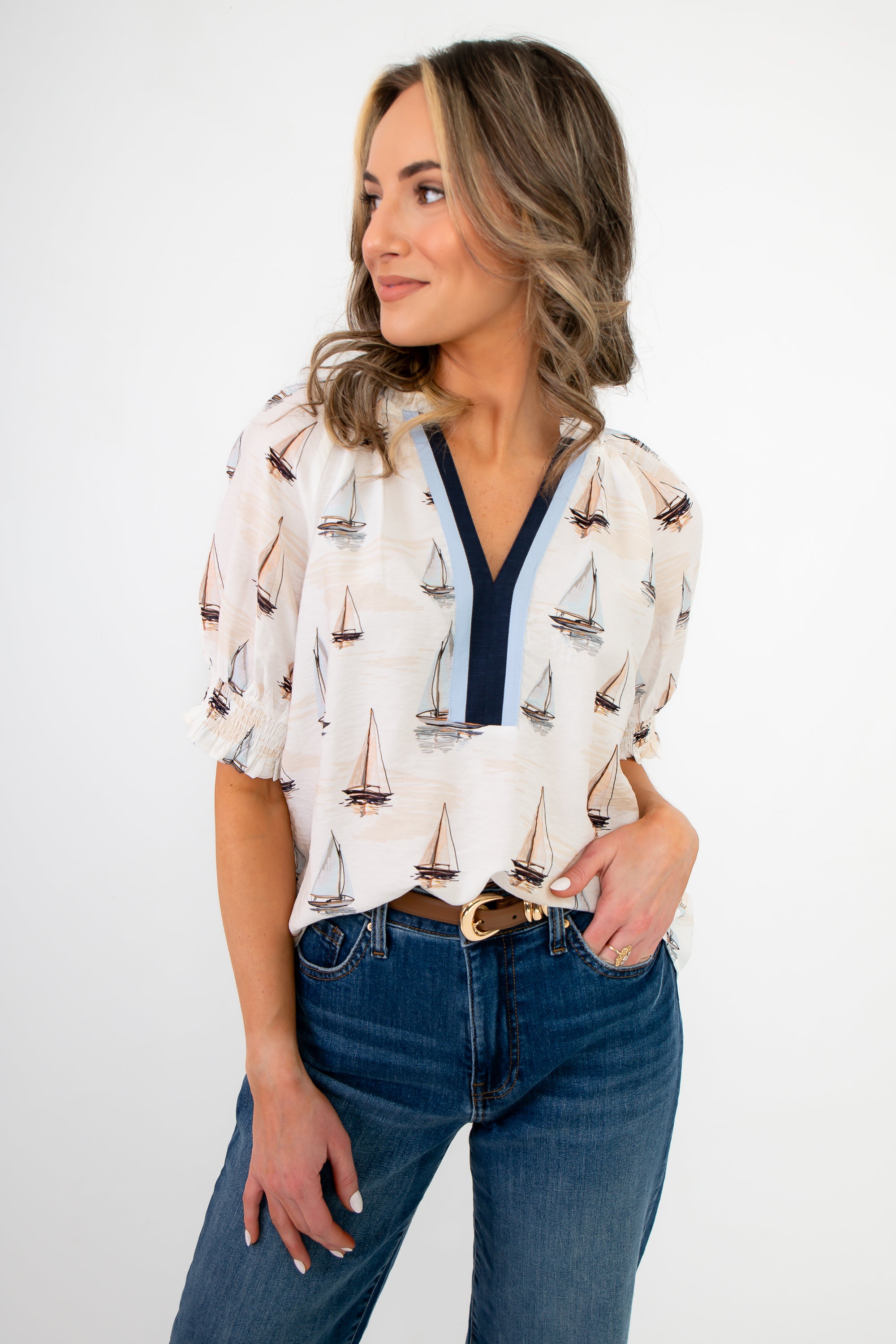 Woman wearing a white blouse with sailboat pattern and blue jeans on a white background