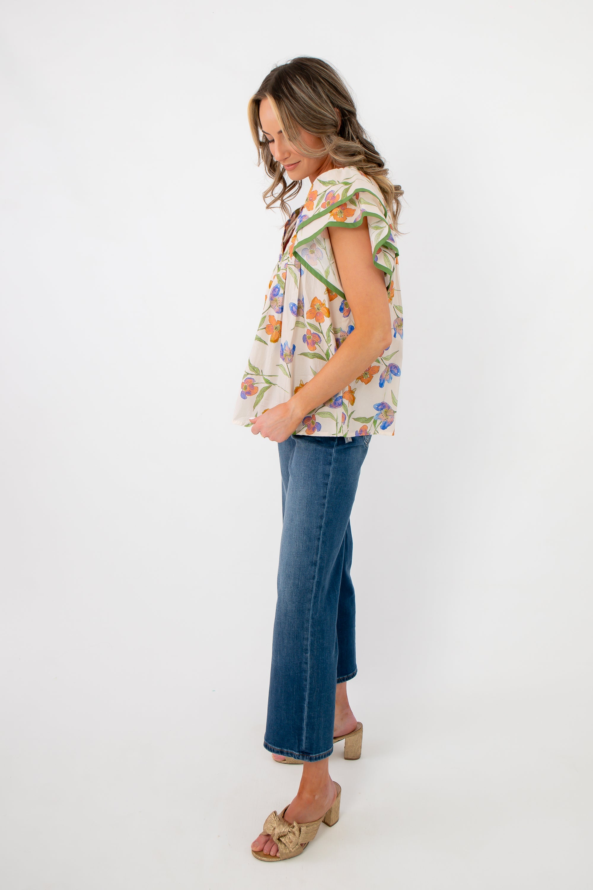 Side view of ecru floral ruffle sleeve blouse with flowy silhouette and green trim, paired with denim for a casual chic look.