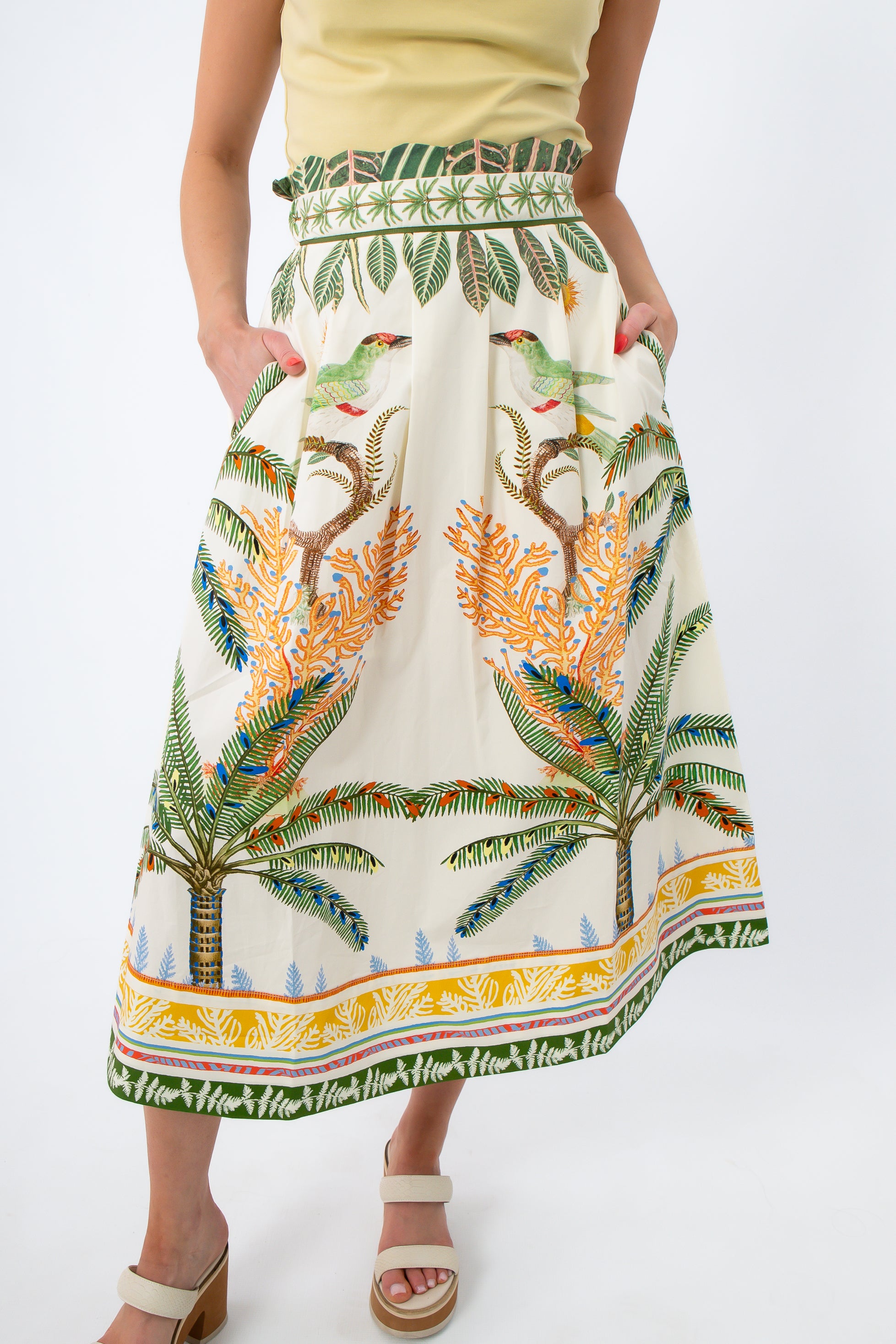 Model wearing tropical print midi skirt with yellow top, showing side pockets and vibrant pattern
