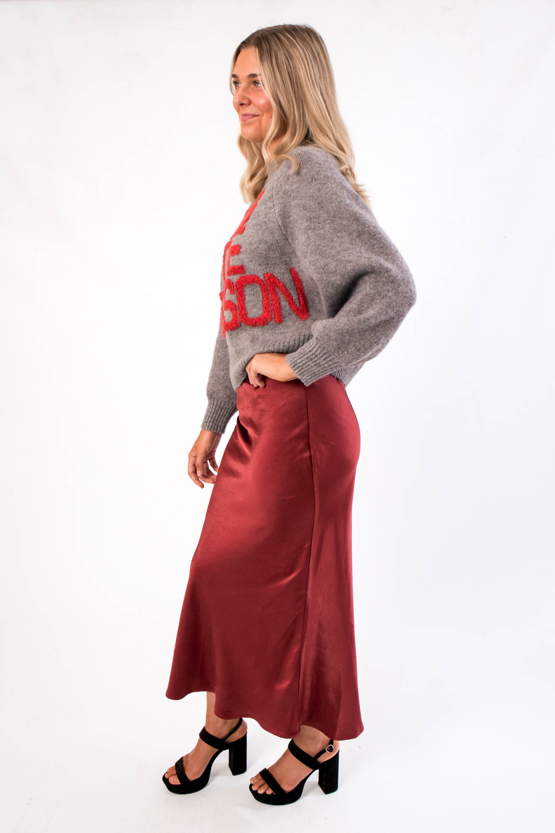 Angled side view of the Cabernet Crush Satin Midi Skirt paired with heels, emphasizing its flowy cut and holiday-ready style.