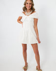 Model wearing white mini dress with off-shoulder design and gold heels for occasion