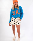 Bold and playful Hit The Slopes Blue & Orange Ski Sweater styled with polka dot shorts and orange knit beanie for a fun winter outfit.