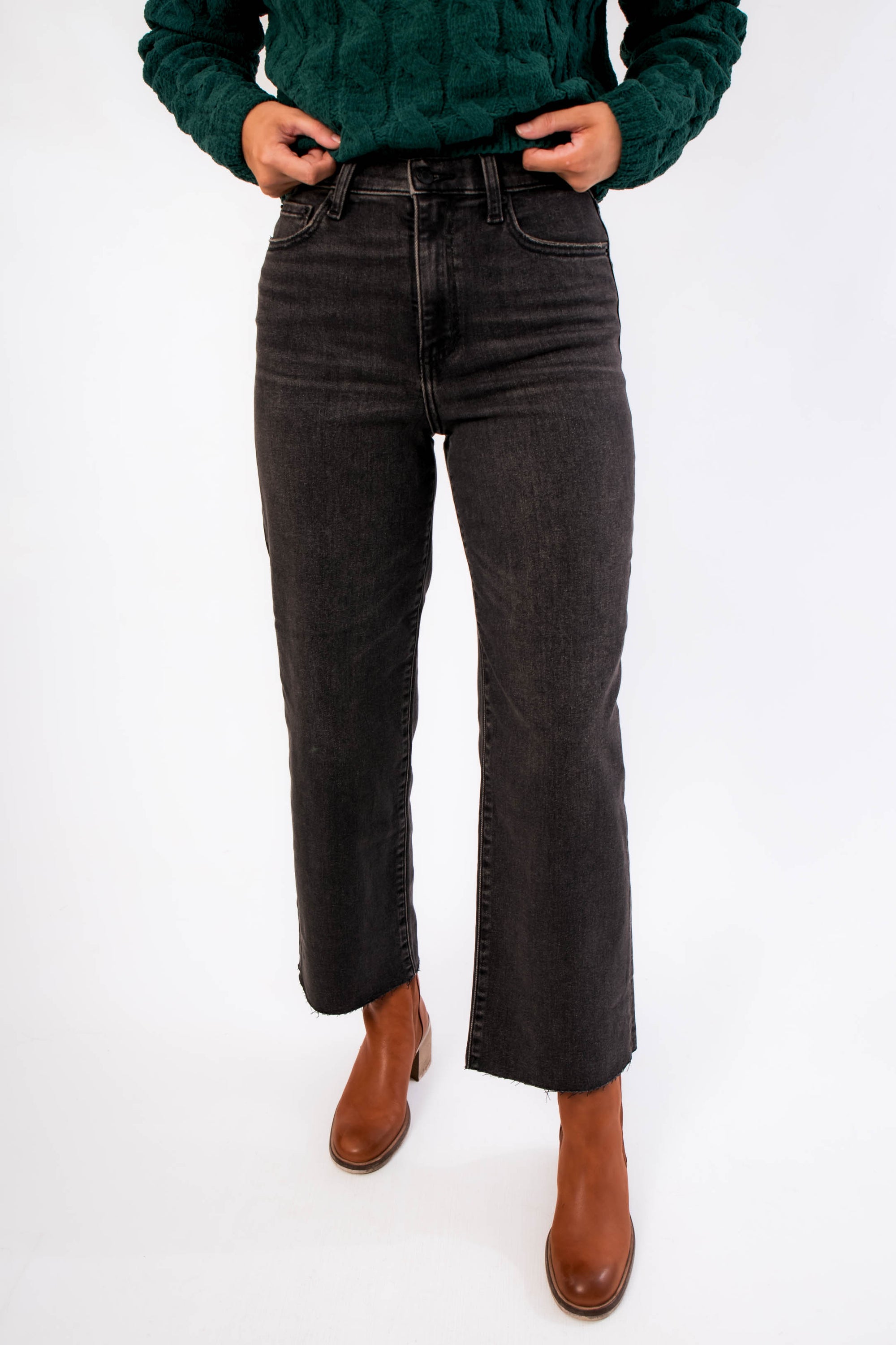 Close-up of Daze Twilight Pleaser High Rise Wide Ankle Jean featuring sustainable faded black denim and raw hem, paired with brown ankle boots.