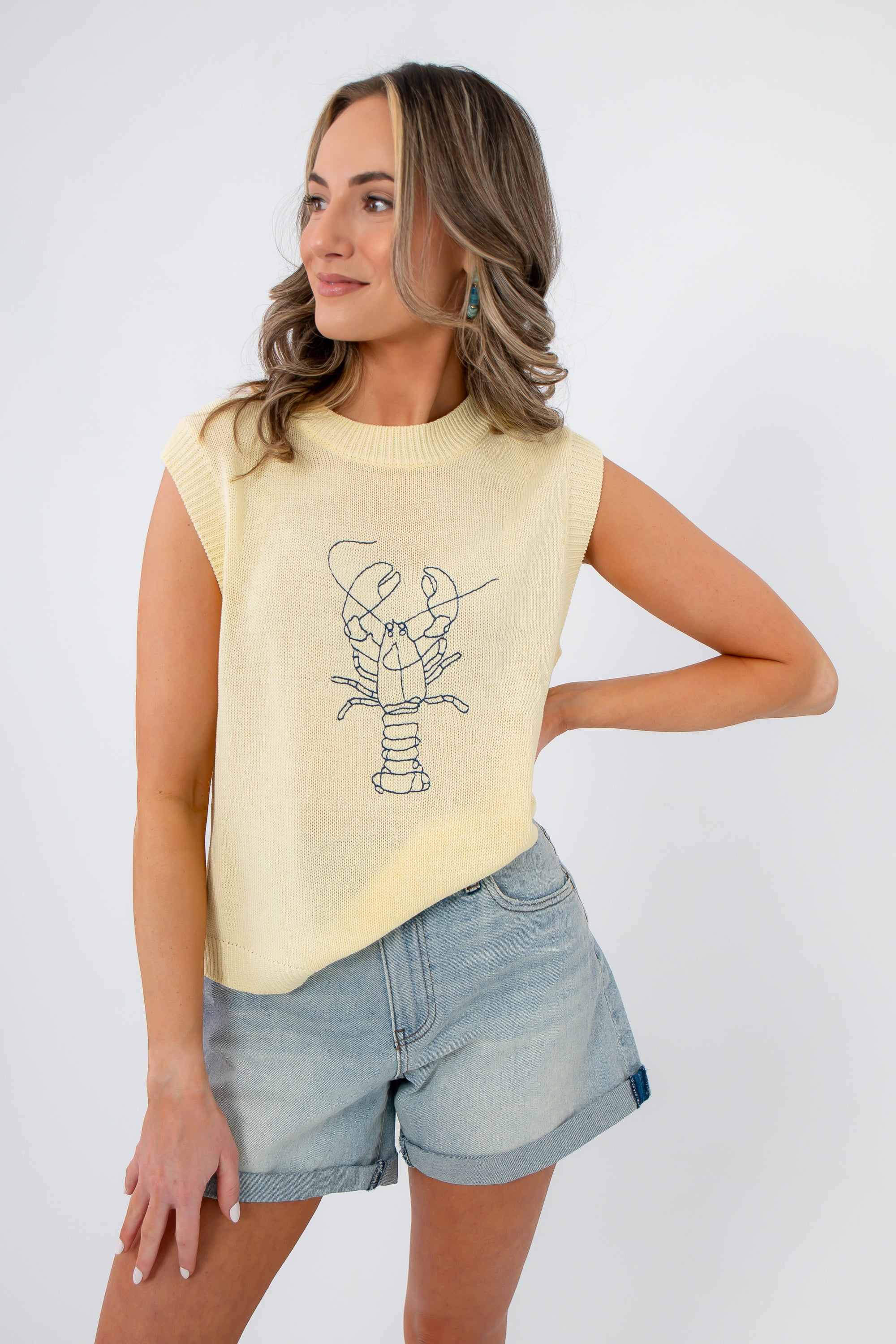 Close-up of sleeveless yellow sweater featuring a lobster embroidery. Lightweight knit top for summer vacations and brunch styling.