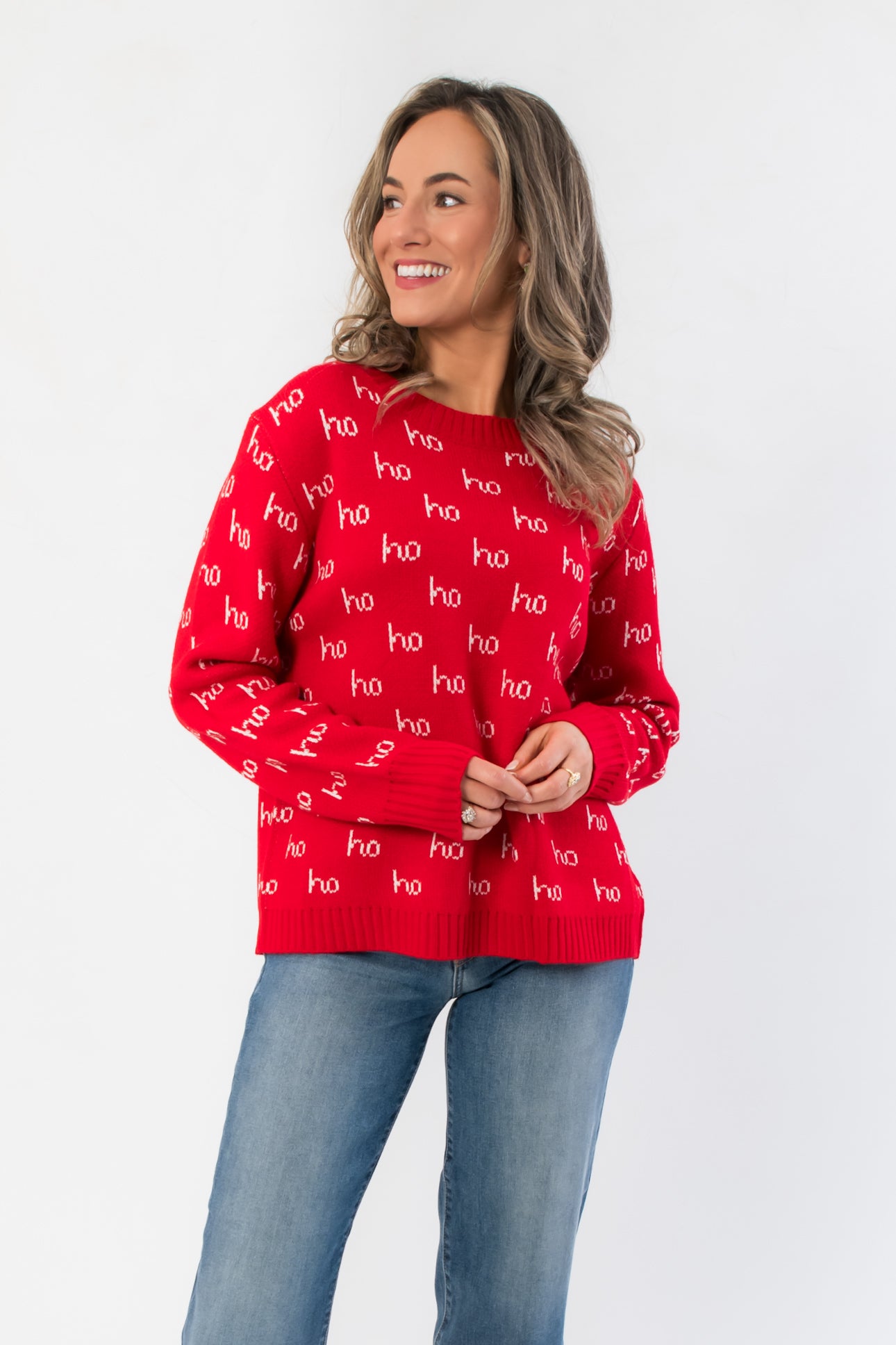 Ho Ho Ho-liday Cheer Red Christmas Sweater with white 'ho' text pattern, long sleeves, and ribbed hem, styled with denim jeans.