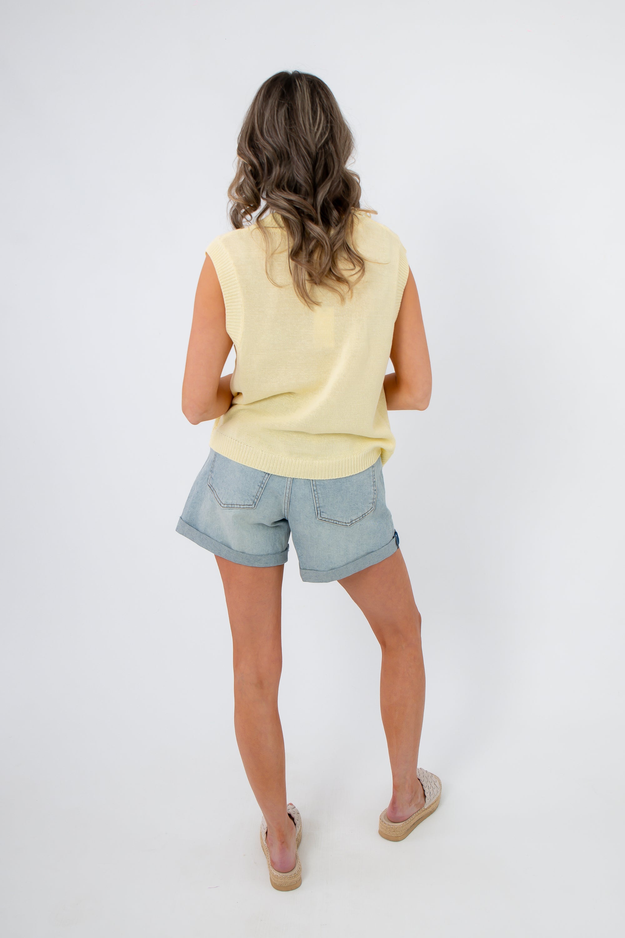 Back view of sleeveless yellow lobster embroidered sweater paired with denim shorts. A relaxed coastal knit for warm-weather wear.