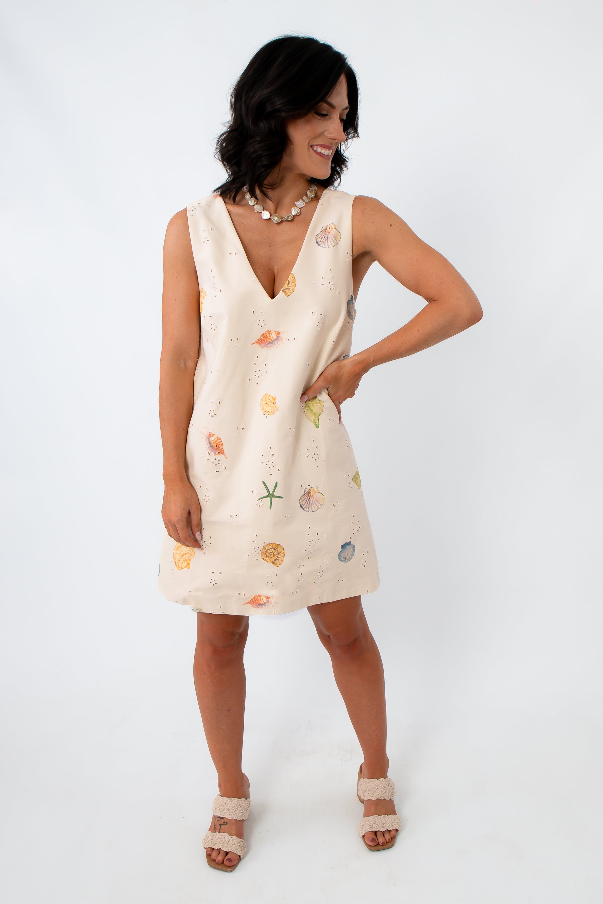 Full-body view of woman in Coastline Romance beach patterned shift dress with shell and starfish print, paired with beige crochet-strap heels.
