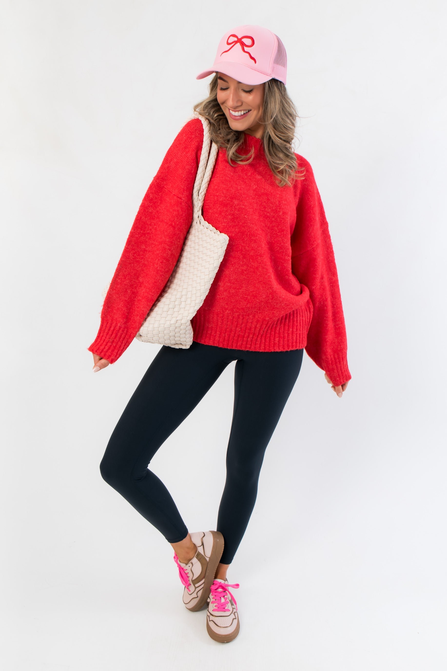 Candied Cherry Red Knit Sweater styled with black leggings, pink cap, and tote bag for a cozy holiday-ready outfit. Ideal for winter lounging.
