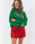 Cozy green Christmas knit sweater with 'Merry' stitched in candy cane stripes, styled festively with a red glitter mini skirt.