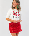 Nutcracker Lane Embroidered Short Sleeve Holiday Sweater for Women featuring festive nutcracker graphics, styled with a red sequin skirt.