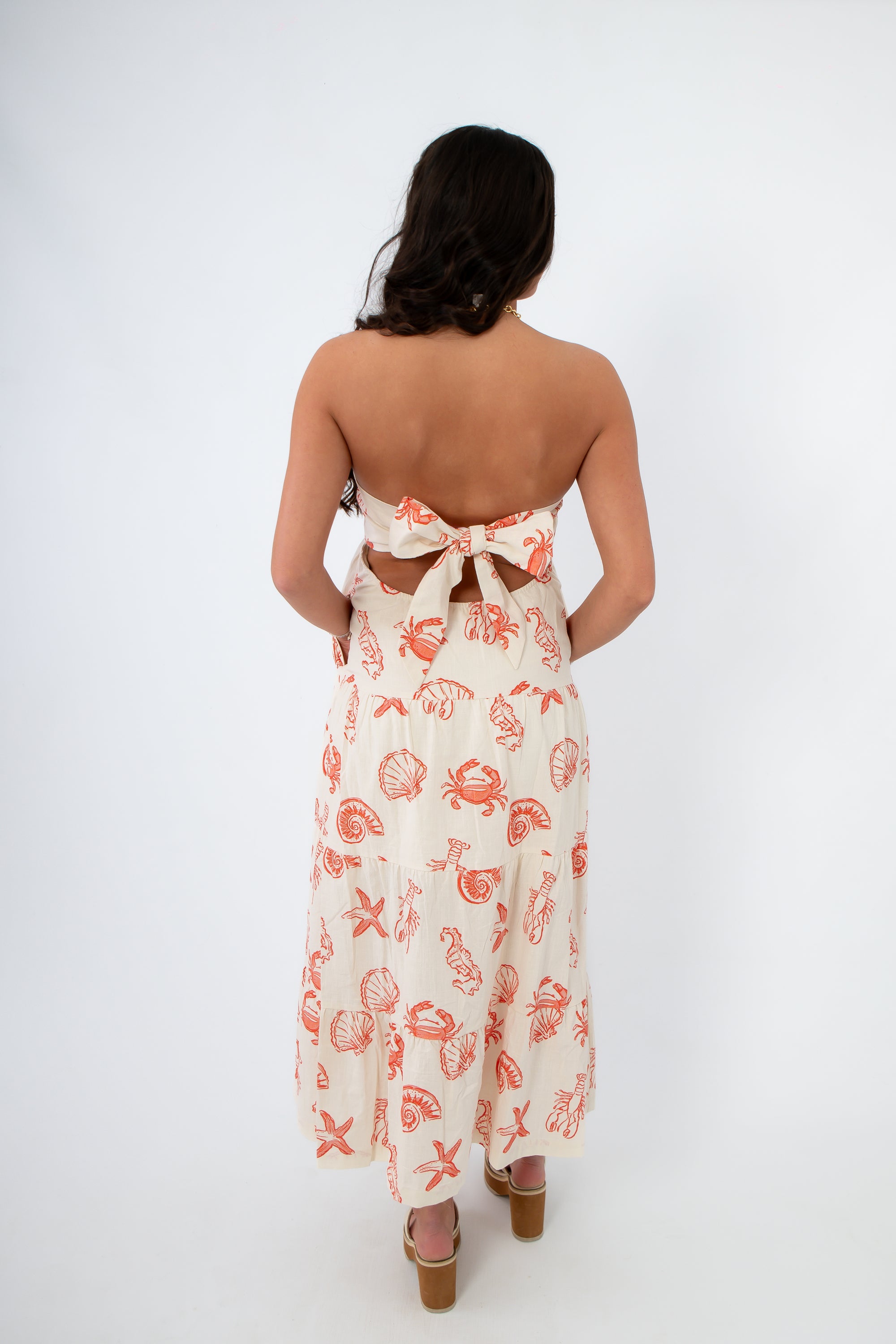 Shelby Red Seashell Printed Strapless Dress with coastal shell motifs in red on cream fabric, featuring a back-tie bow and flowy midi length.