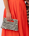 Two women posing together against a white studio background. The woman on the left wears a bright orange sleeveless maxi dress and holds a zebra-print clutch.