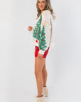 Side view of Cozy & Chic Christmas Tree Plush Cardigan showing festive tree pattern on sleeves, paired with red skirt and cream boots.