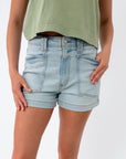Close-up of light wash denim shorts with large front pockets, high waist, and rolled hem, worn with a green top, showcasing summer denim fashion