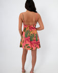 Back view of Cabana Nights Tropical Printed Mini Dress in coral with pink and green leaf pattern, featuring open back and tie detail.