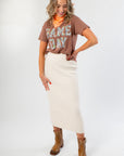 Model wearing It's Gameday Camo Crop Graphic Tee – Stylish Neutral Crop Top with bold camo lettering, paired with a cream knit skirt and brown boots.