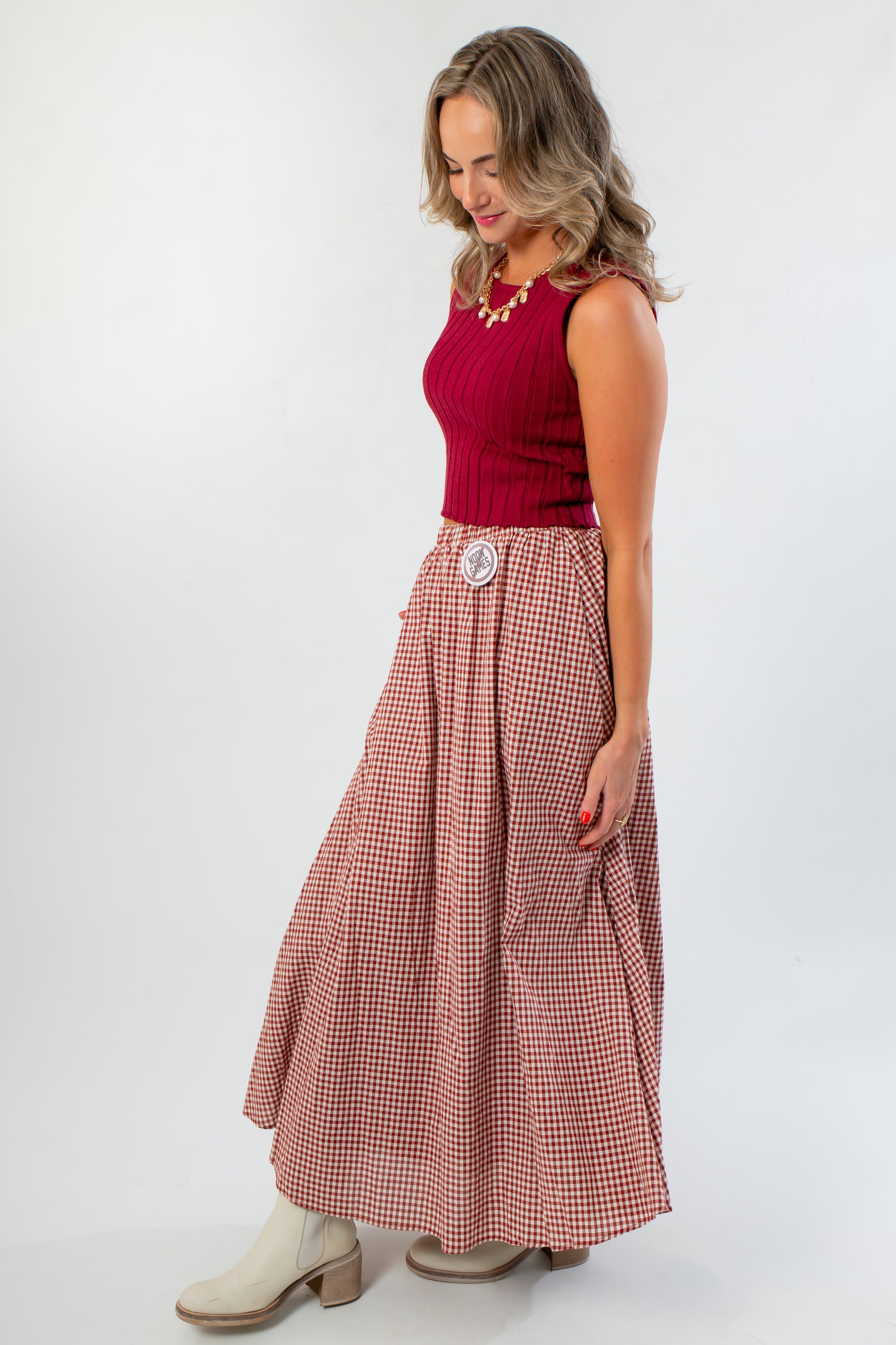 Side view of Wine &amp; Dine Sleeveless Sweater in wine rib knit, styled with a checkered skirt and ankle boots for a cozy fall ensemble.