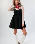 Elegant Black Bubble Hem Mini Dress with ruched bust and tie straps, paired with white boots and red bandana for a stylish casual outfit.
