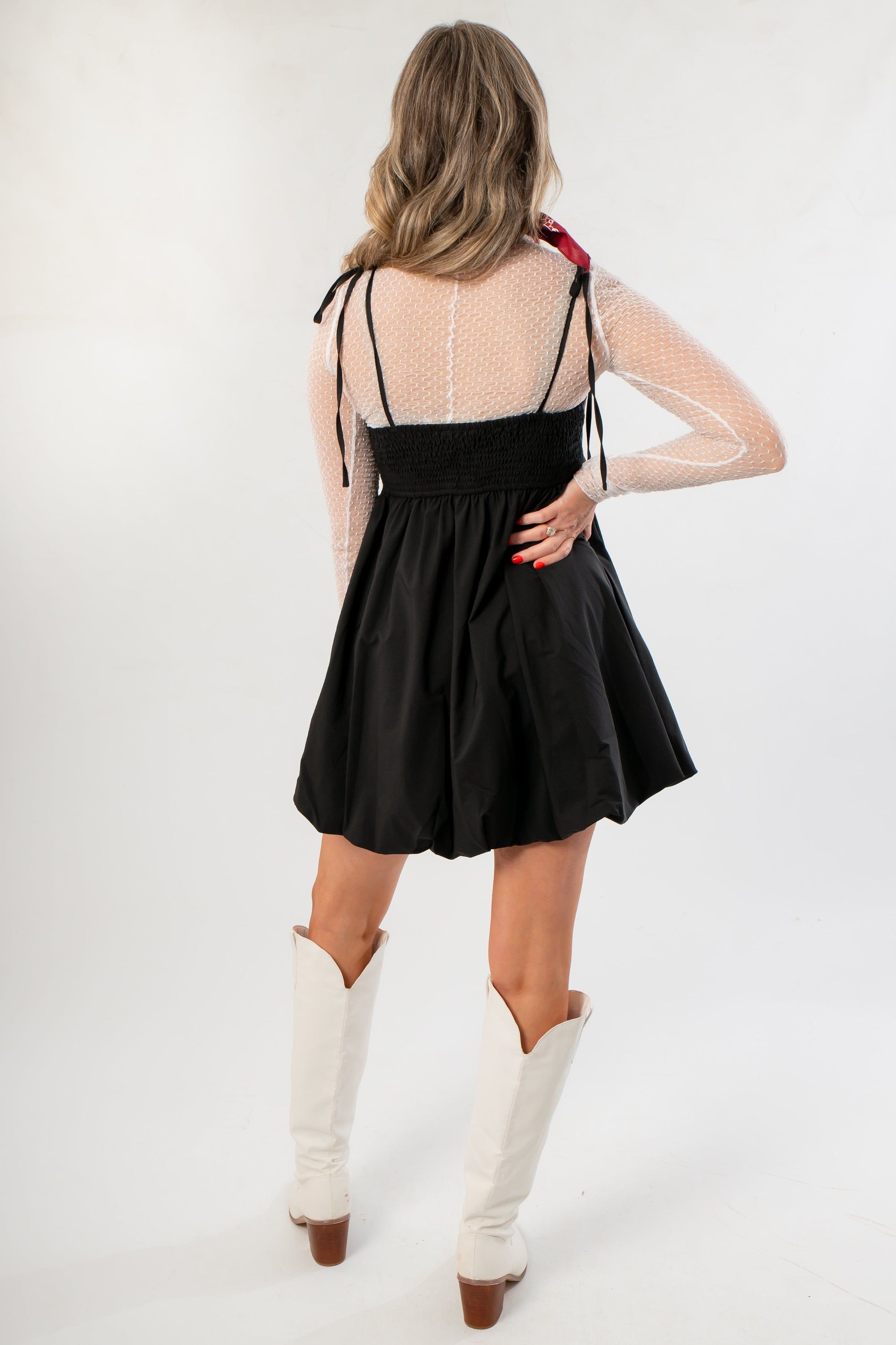 Back view of Black Hem Mini Dress with smocked bodice and bubble skirt, styled with mesh sleeves and white boots for a modern flair.